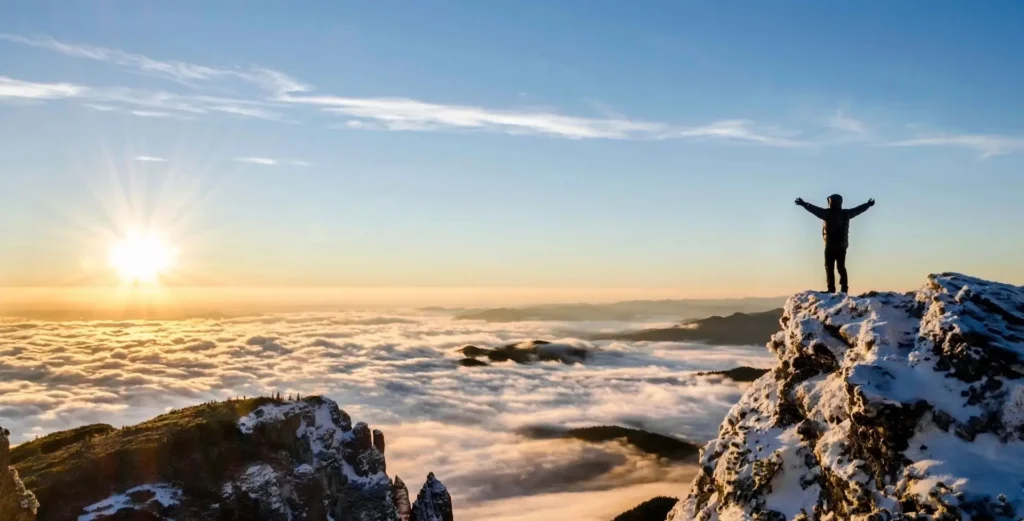 Snowy mountain peaks above a sea of clouds at sunset.